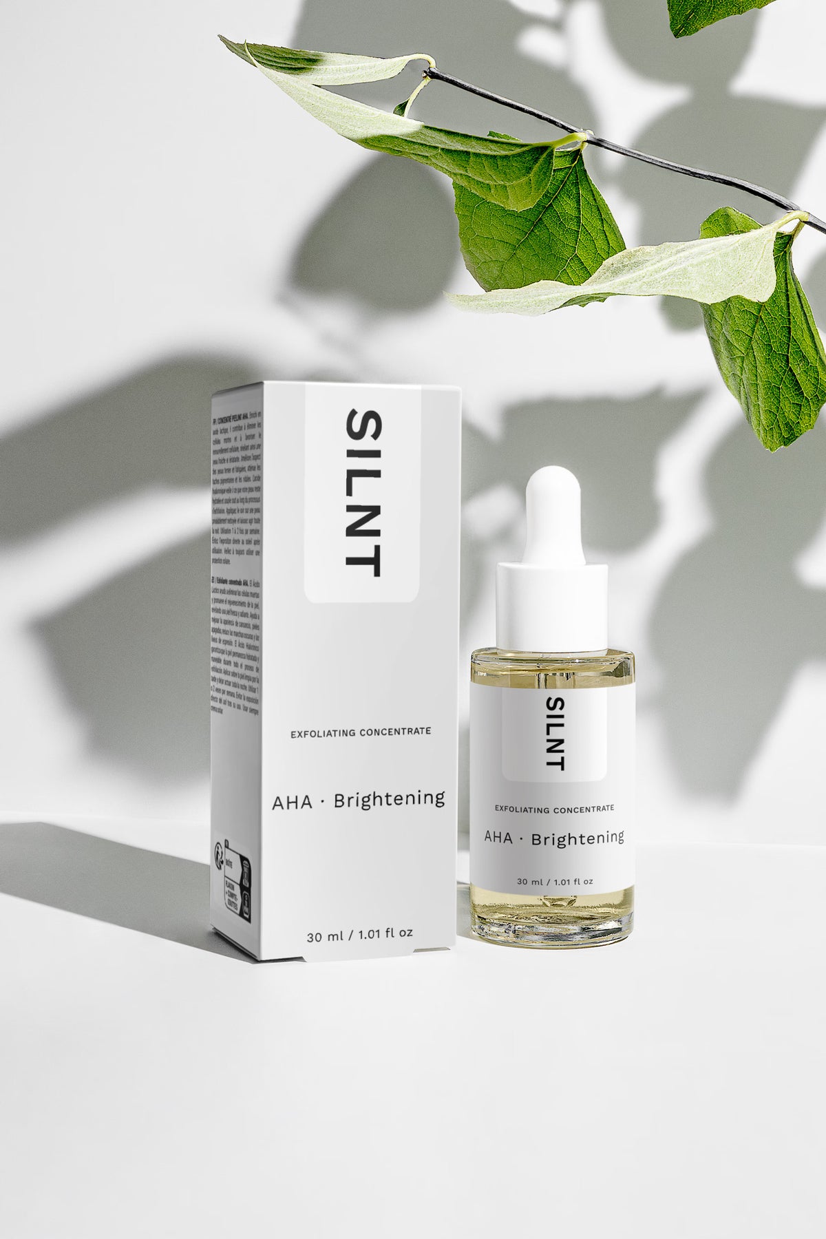 SILNT Exfoliating Concentrate bottle beside its carton with soft leaf shadows on a light grey background