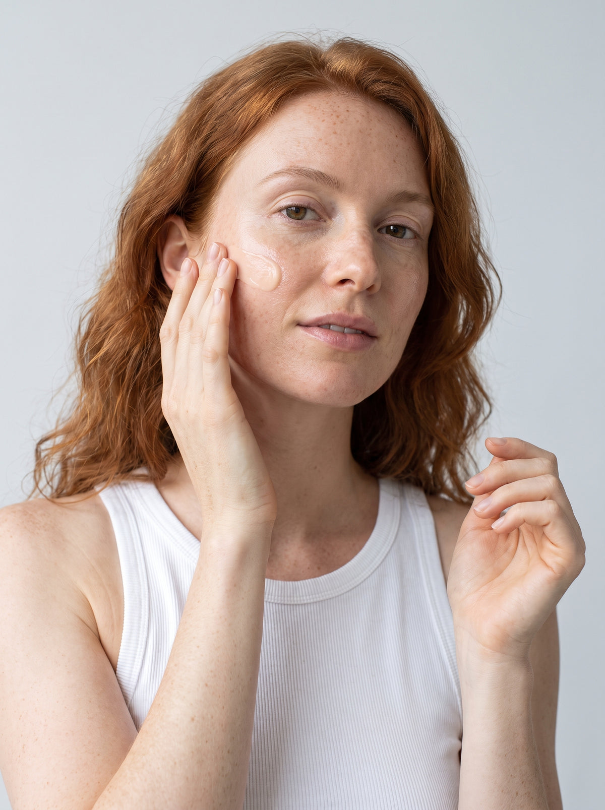 Red-haired woman smoothing SILNT Brightening Cream onto her face