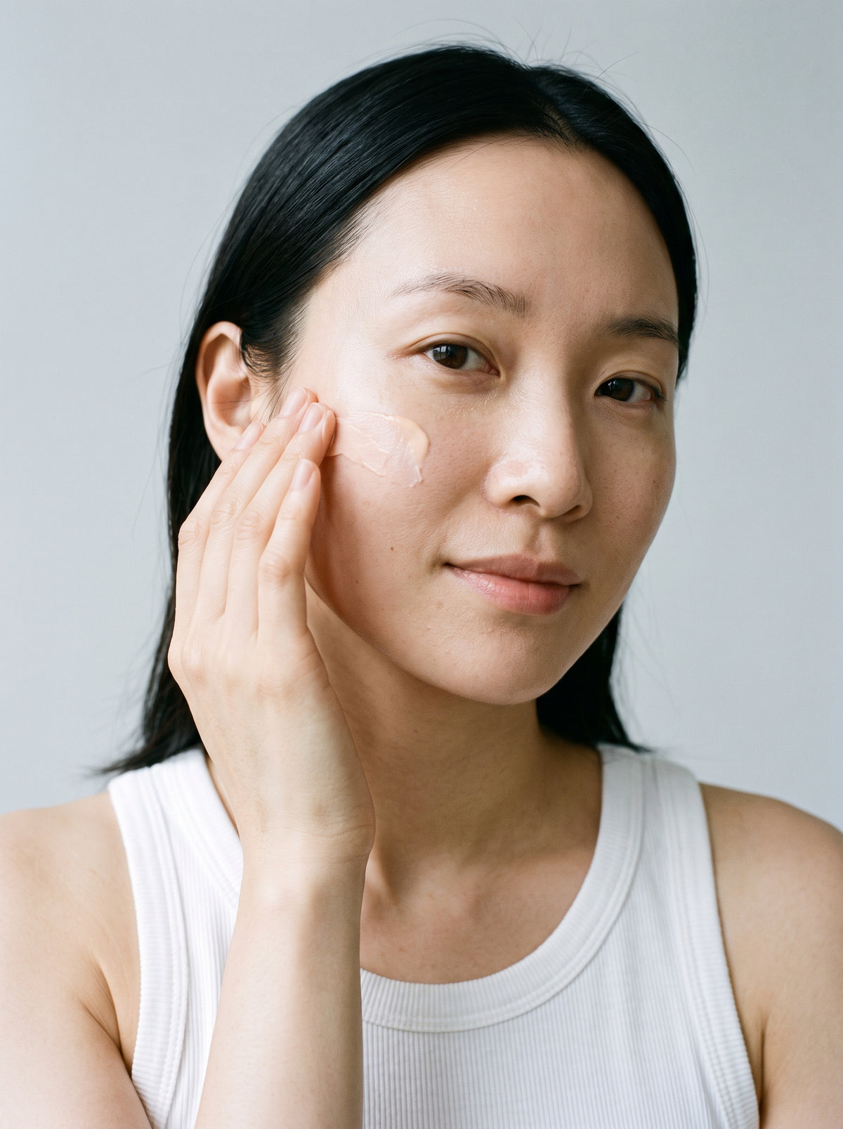 Woman in a white tank top applying SILNT Brightening Cream to her cheek