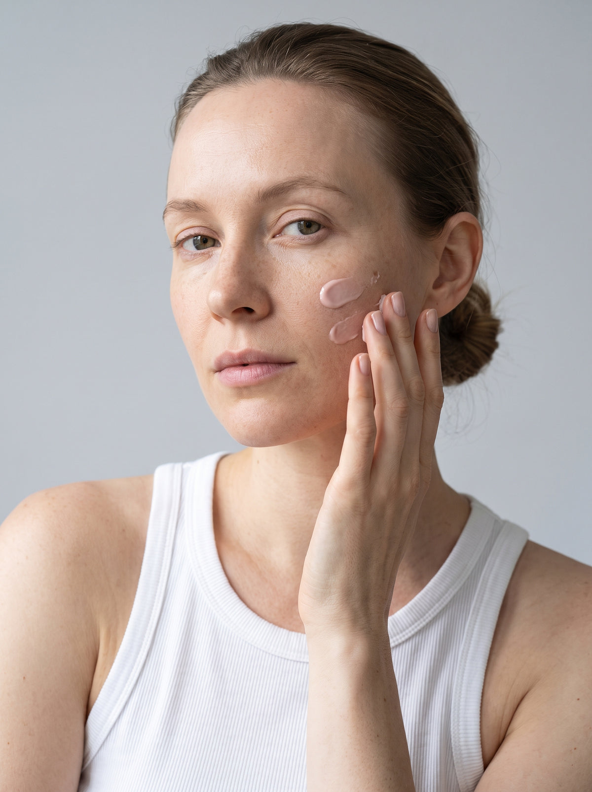 SILNT Peptide Serum smoothed along a model's cheekbone, white tank top, light grey background