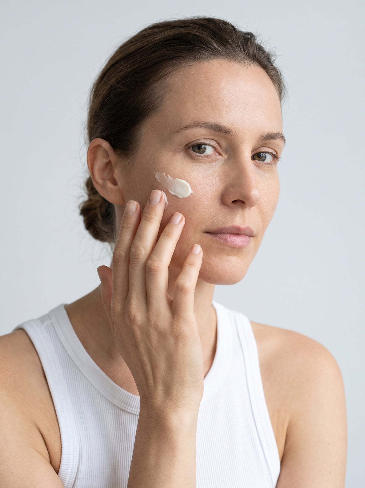 SILNT Day Cream smoothed along a model's cheekbone, white tank top, light grey background