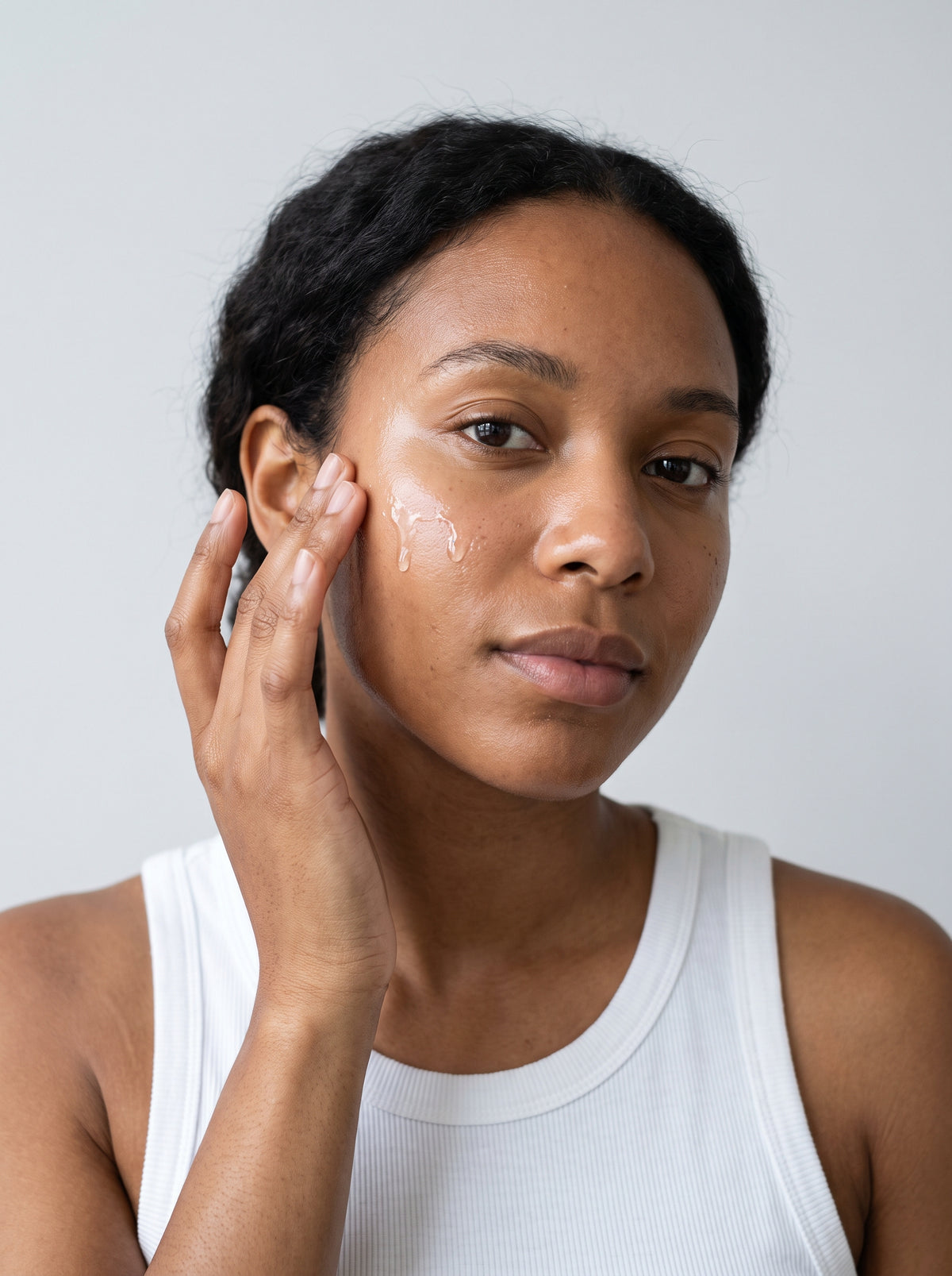 SILNT Exfoliating Concentrate smoothed along a model's cheekbone, white tank top, light grey background