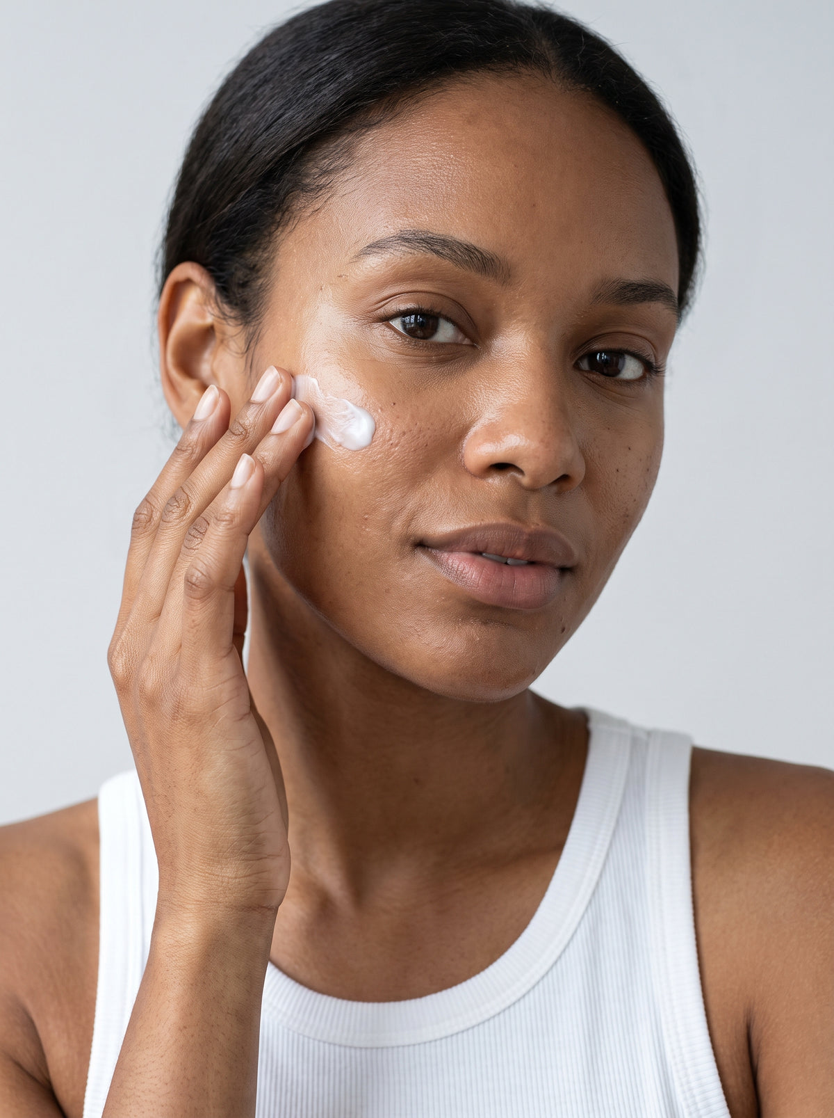 SILNT Daily Moisturizer smoothed along a model's cheekbone, white tank top, light grey background