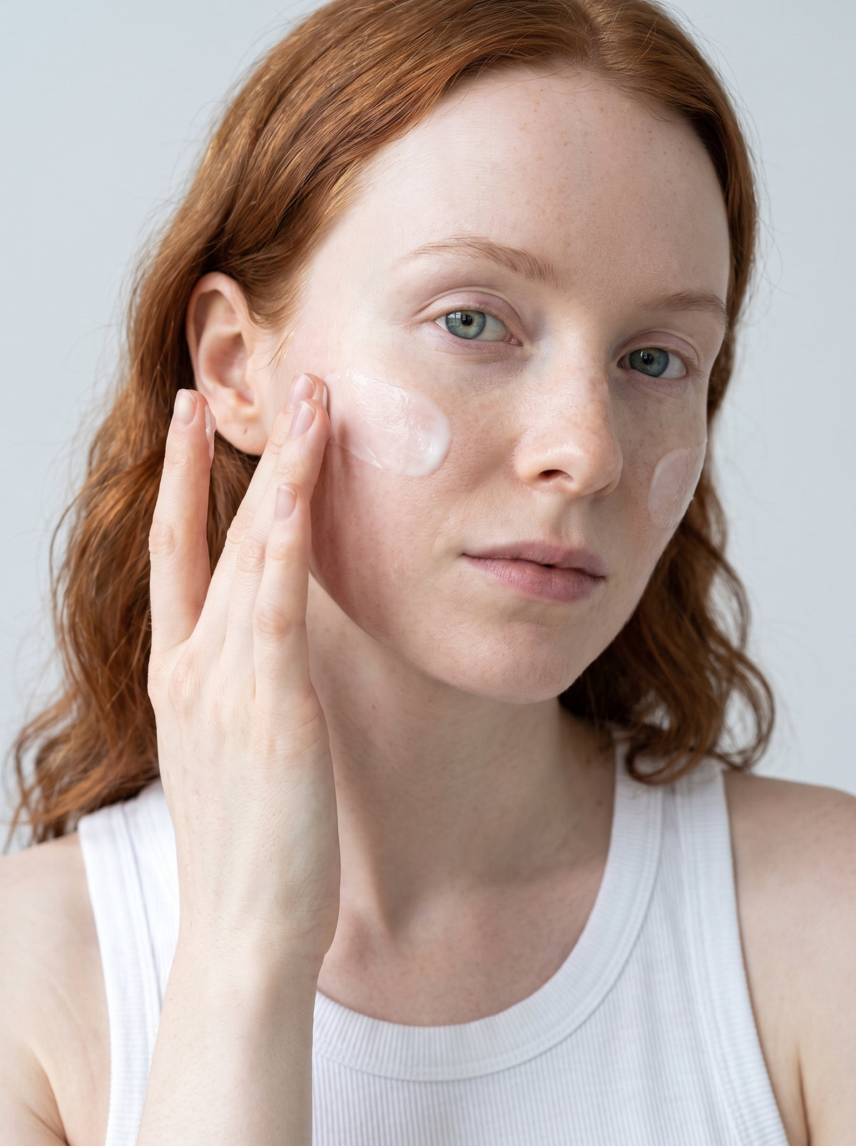 SILNT Rich Cream applied to a model's cheek with her fingertips, white tank top, light grey background