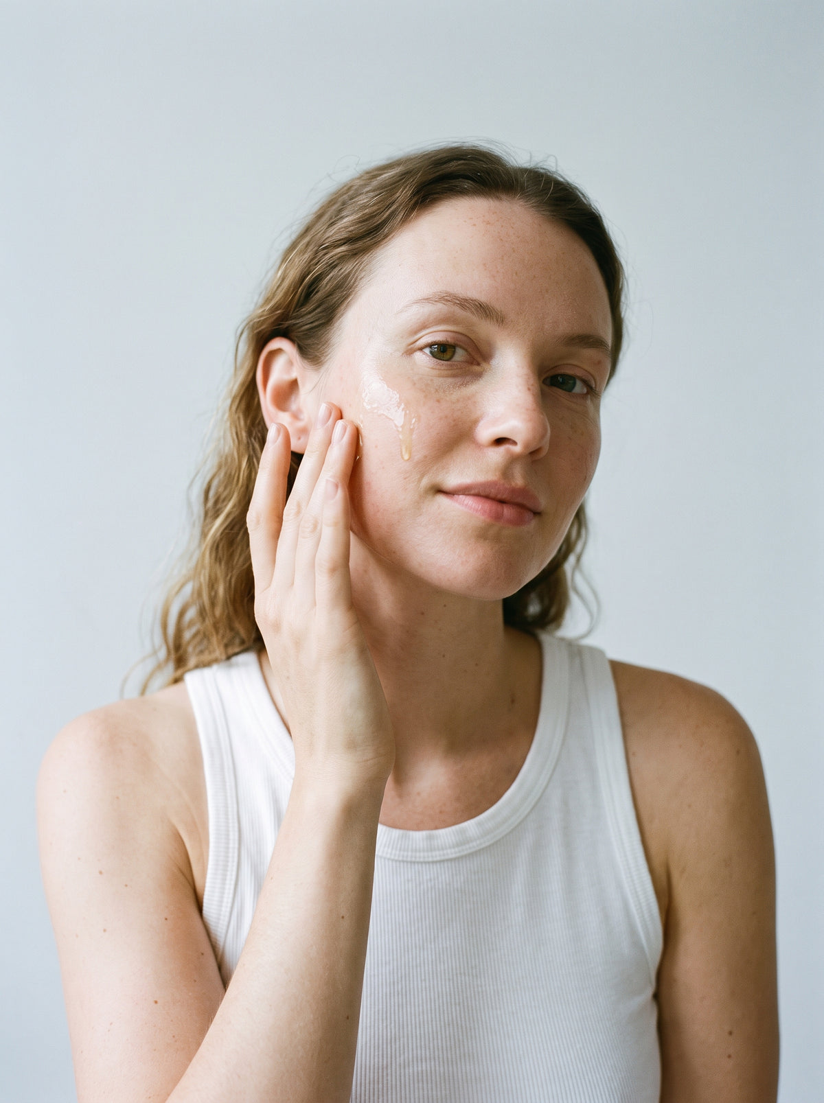 SILNT Bakuchiol Serum smoothed along a model's cheekbone, white tank top, light grey background