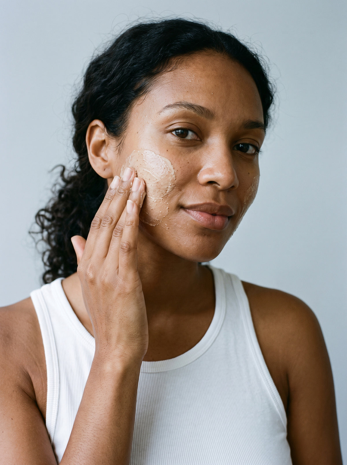 Woman in a tank top applying SILNT Brightening Polish to her face