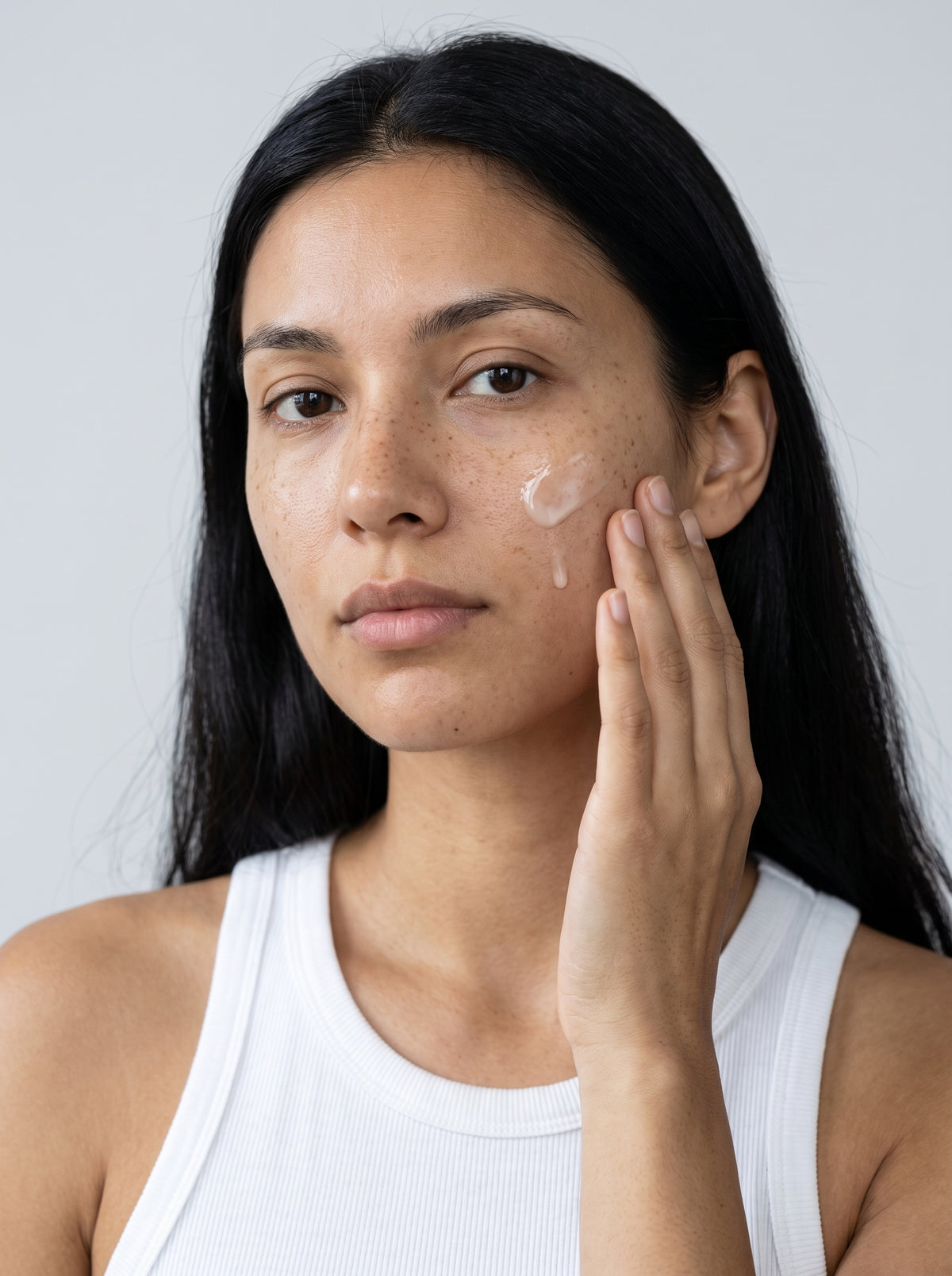 SILNT Brightening Serum smoothed along a model's cheekbone, white tank top, light grey background