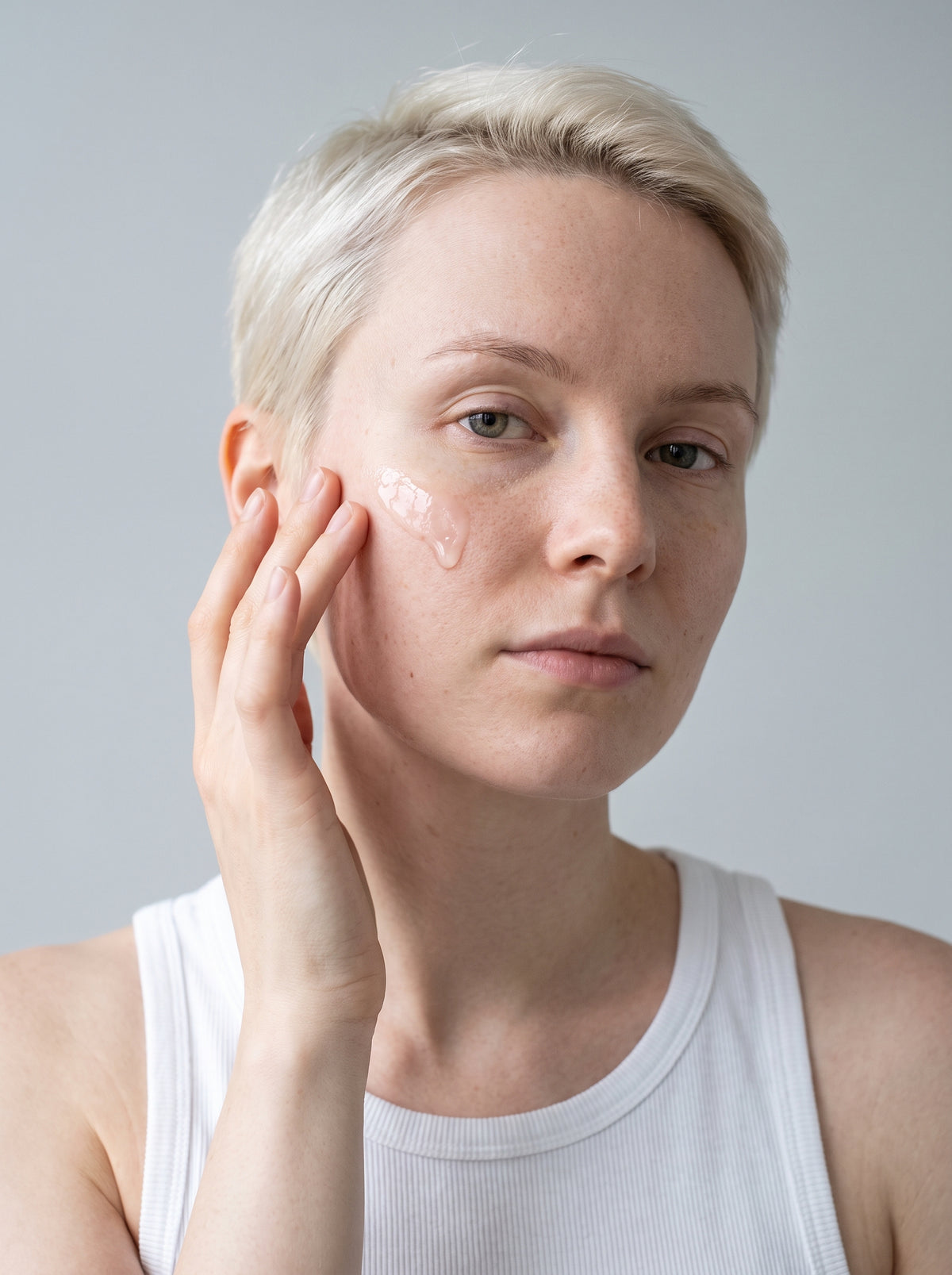 SILNT Hydrating Serum applied to a model's cheek with her fingertips, white tank top, light grey background