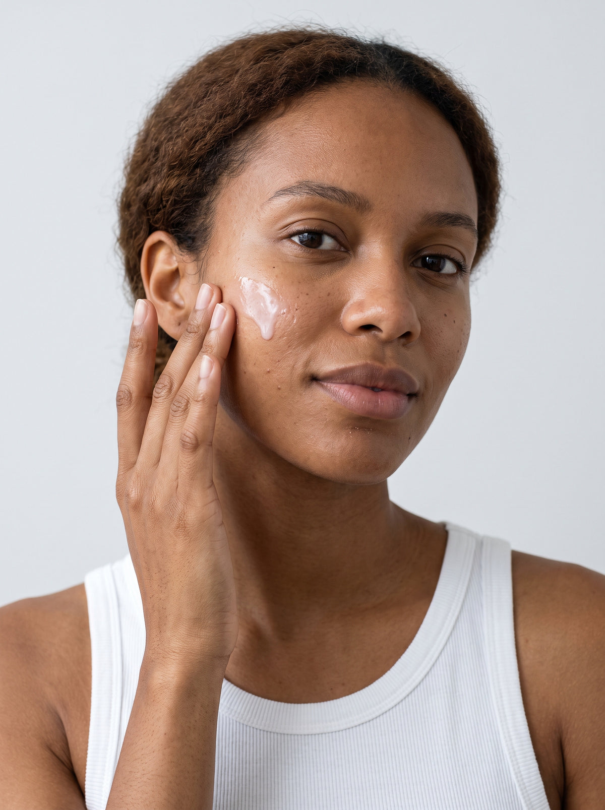 Woman in a white tank top applying SILNT Exosome Serum to her cheek
