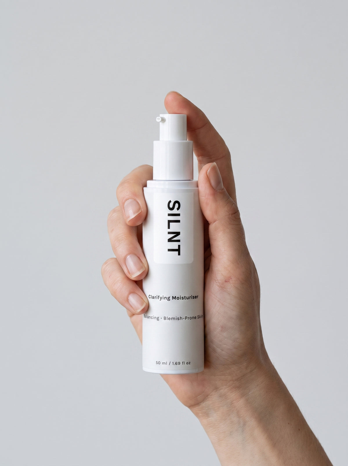 SILNT Clarifying Moisturiser bottle held upright in one hand against a light grey background