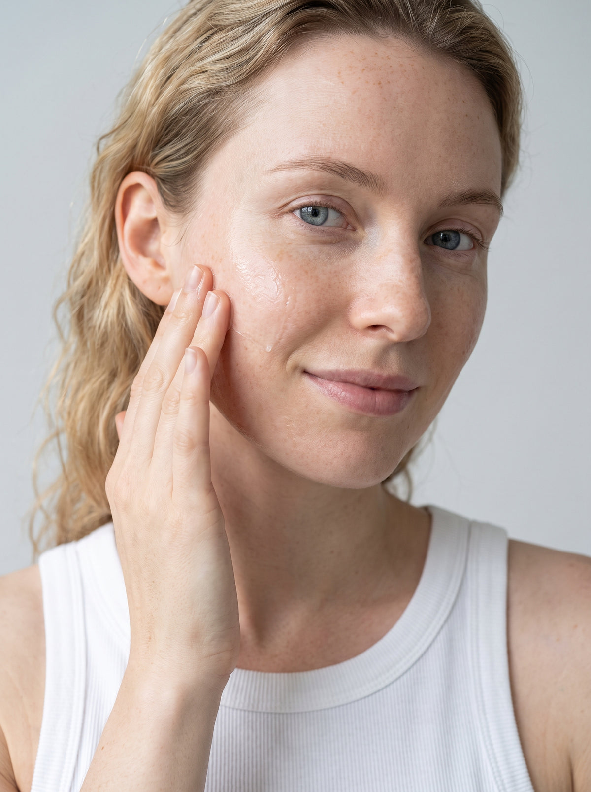 SILNT Cleansing Oil massaged over a model's cheek with her fingers, white tank top, light grey background