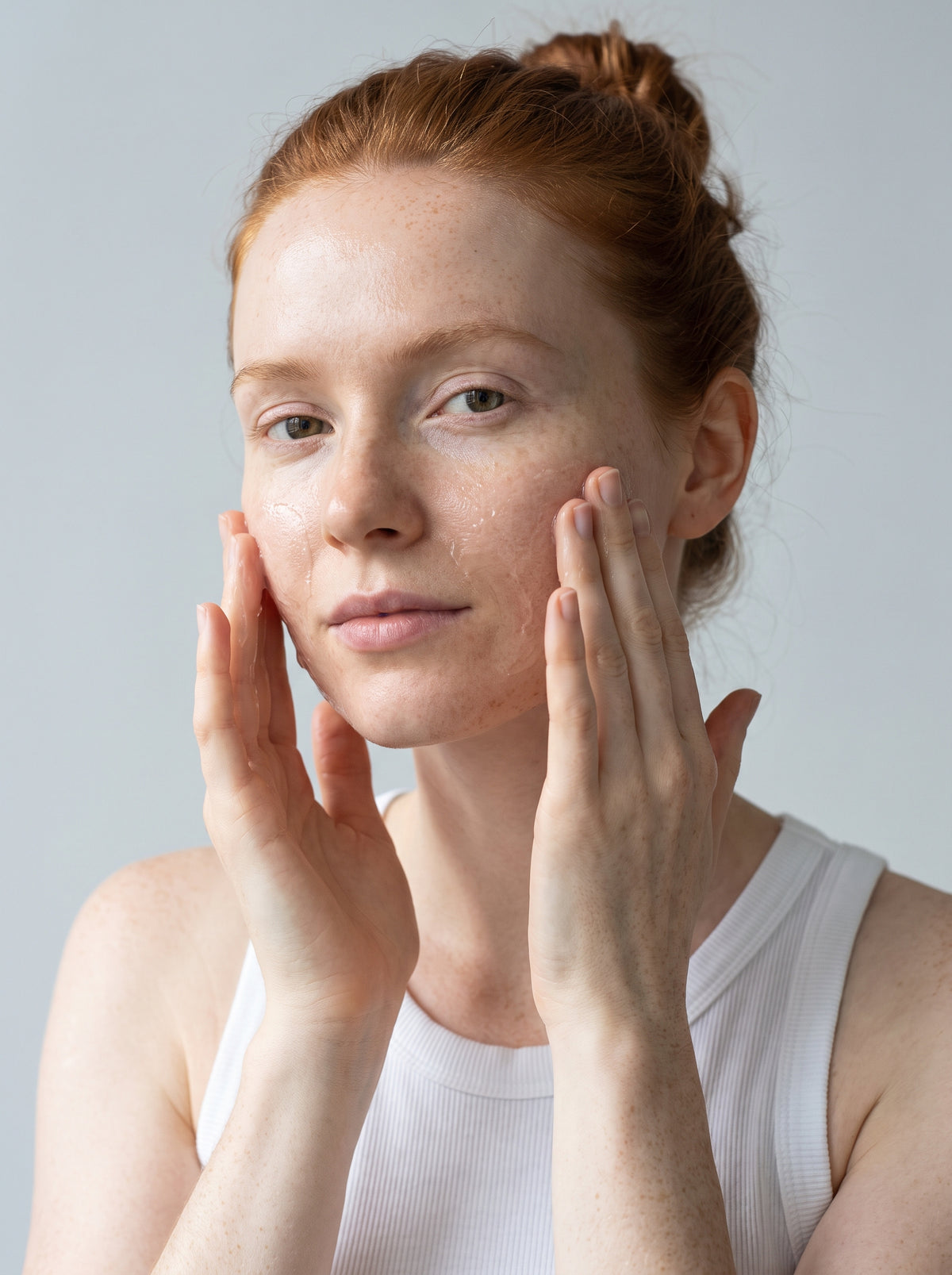 SILNT Clarifying Cleanser massaged over a model's cheeks with both hands, white tank top, light grey background