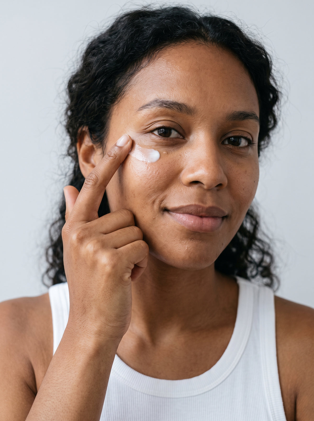 SILNT Eye Cream patted under a model's eye with her ring fingertip, white tank top, light grey background
