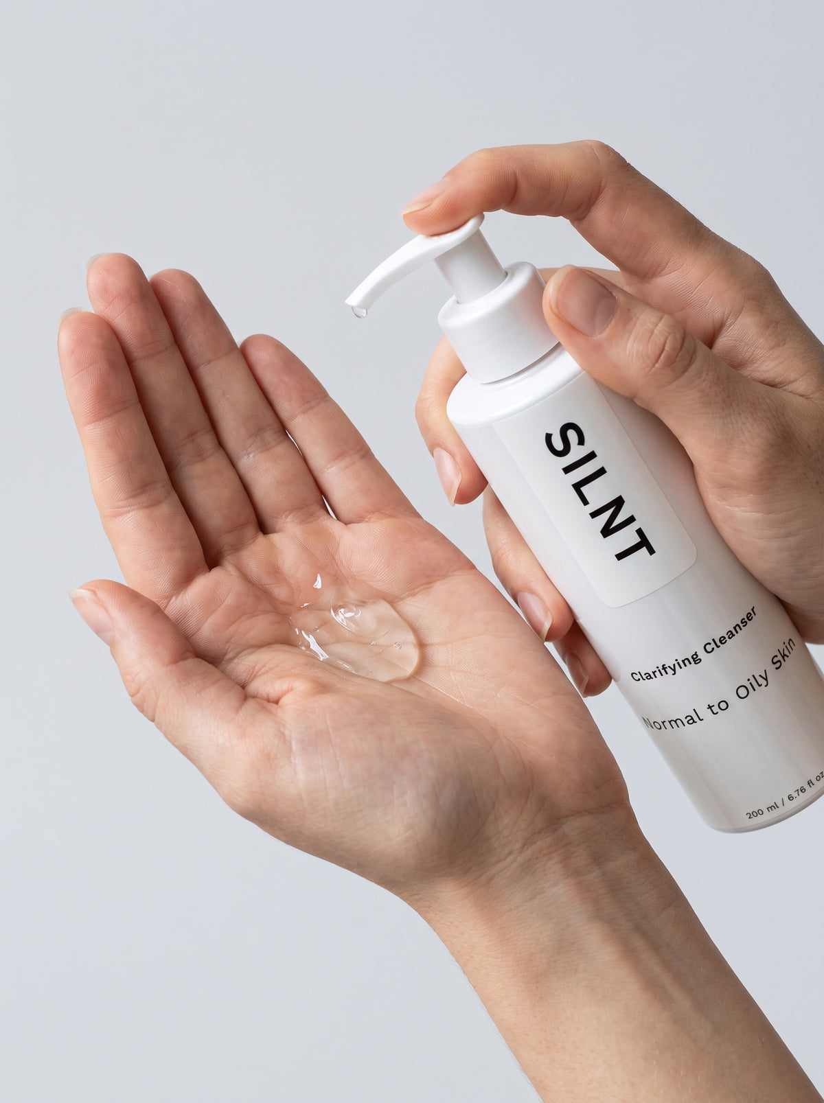 SILNT Clarifying Cleanser clear gel dispensed into an open palm from the pump bottle, light grey background