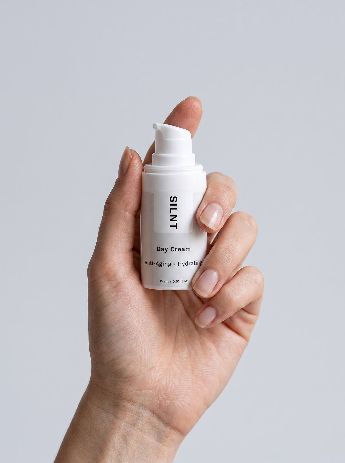 SILNT Day Cream travel size bottle held upright in one hand, showing its 15 ml size, light grey background