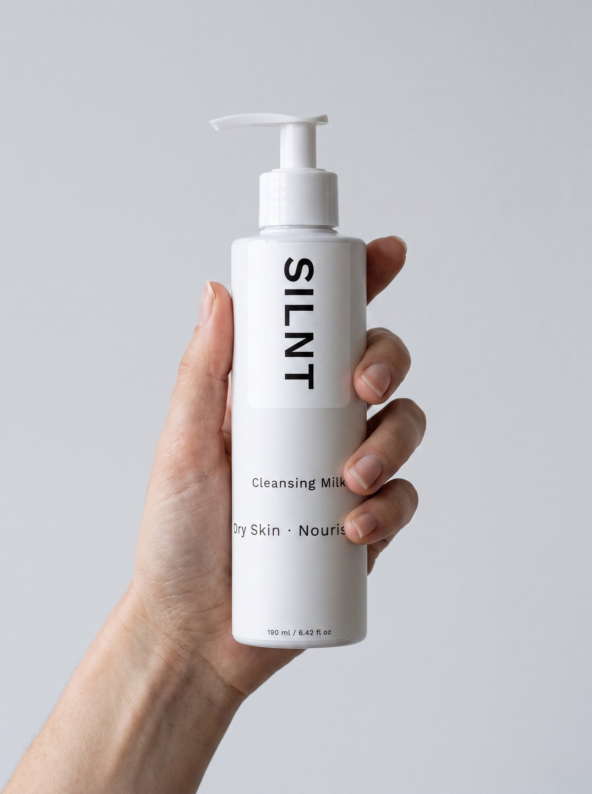 SILNT Cleansing Milk bottle held upright in one hand, showing its 190 ml size, light grey background