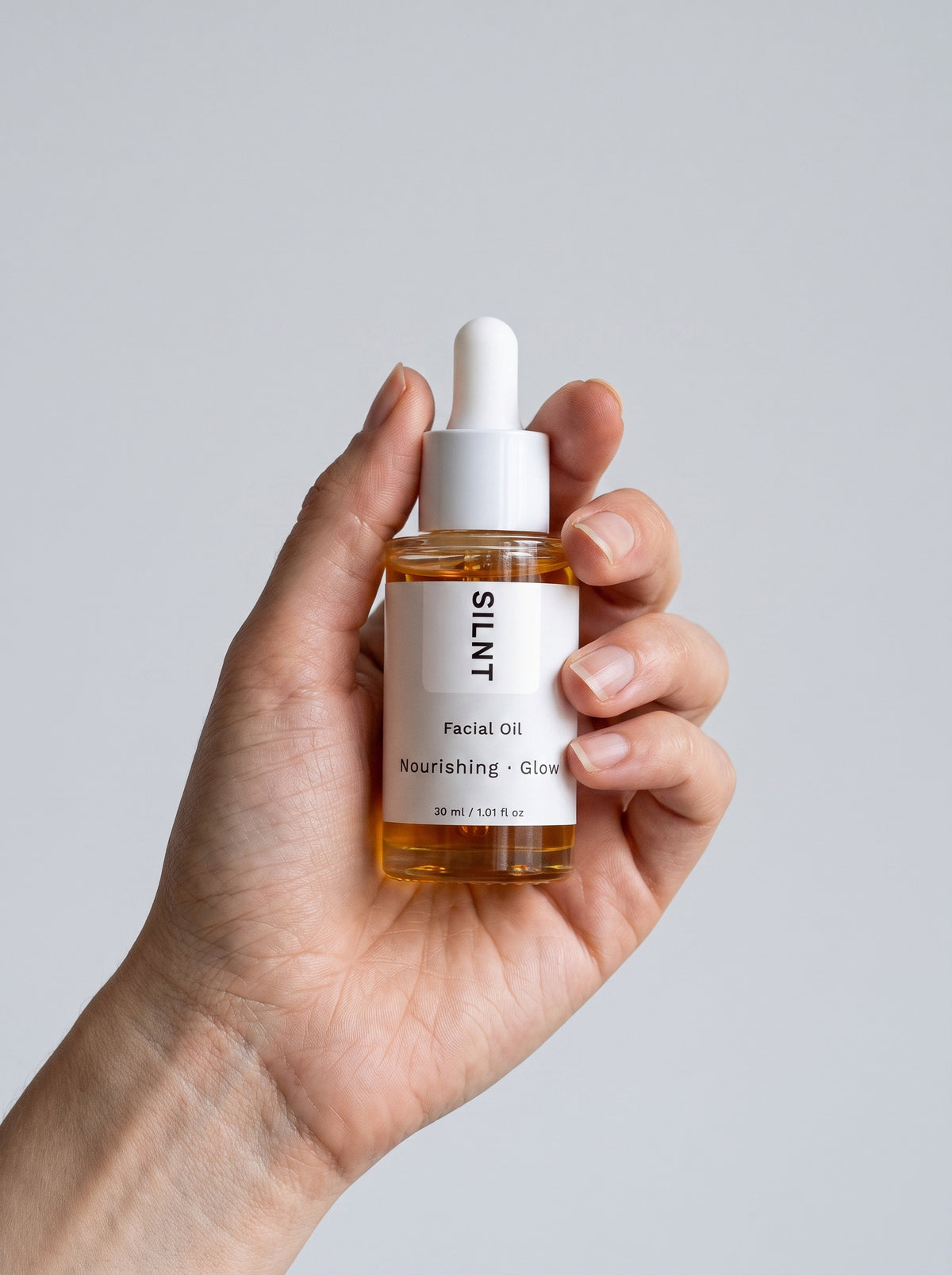 SILNT Facial Oil bottle held upright in one hand against a light grey background