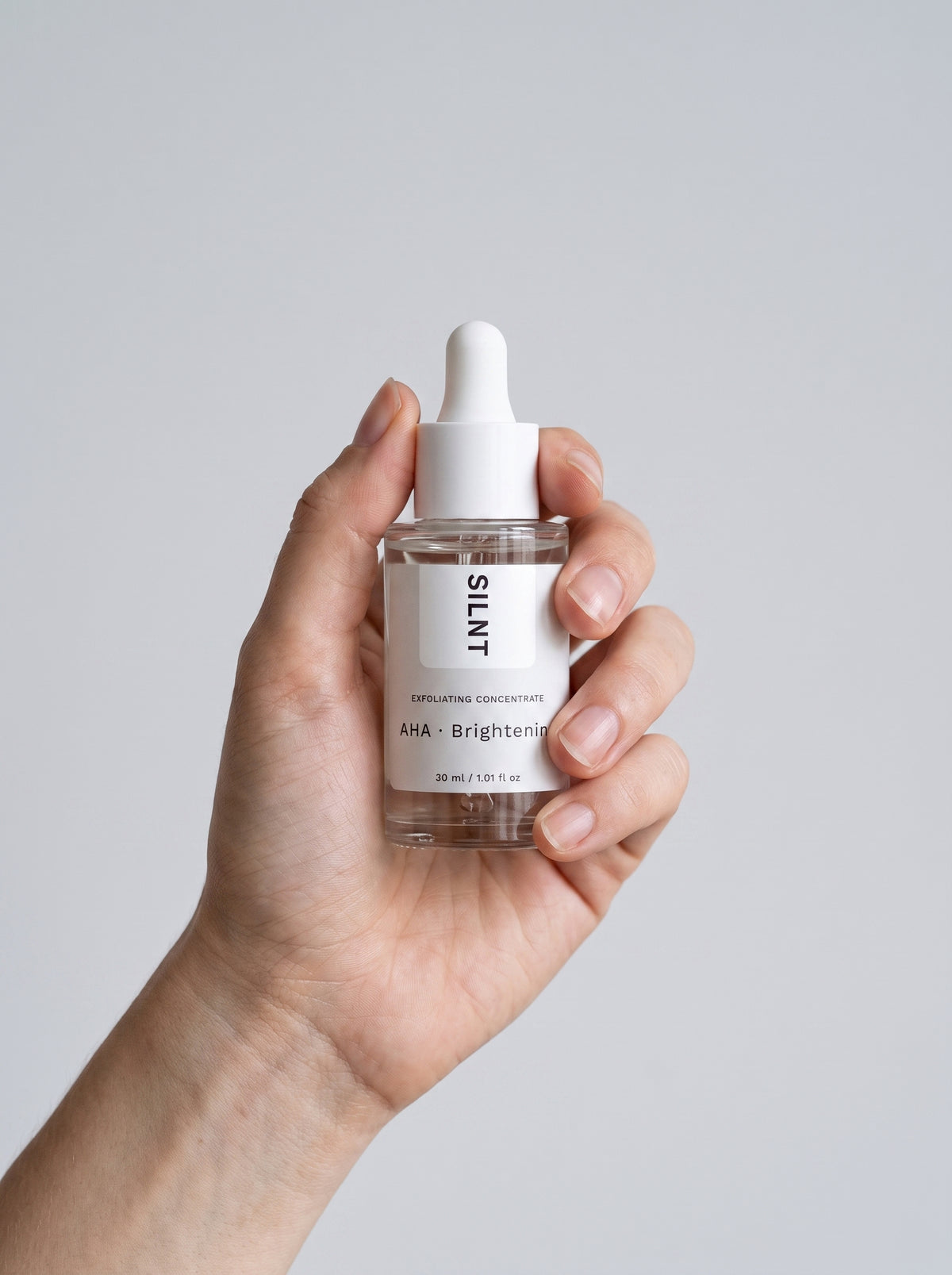 SILNT Exfoliating Concentrate bottle held upright in one hand against a light grey background