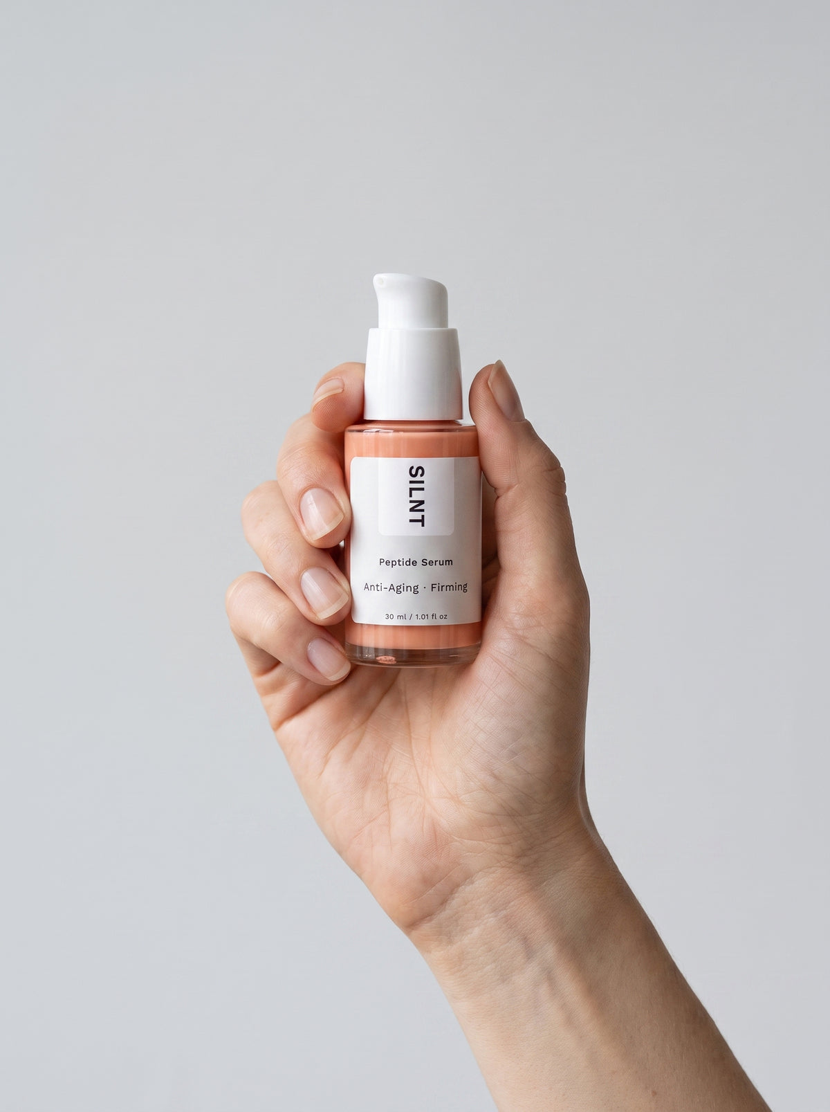 SILNT Peptide Serum bottle held upright in one hand against a light grey background