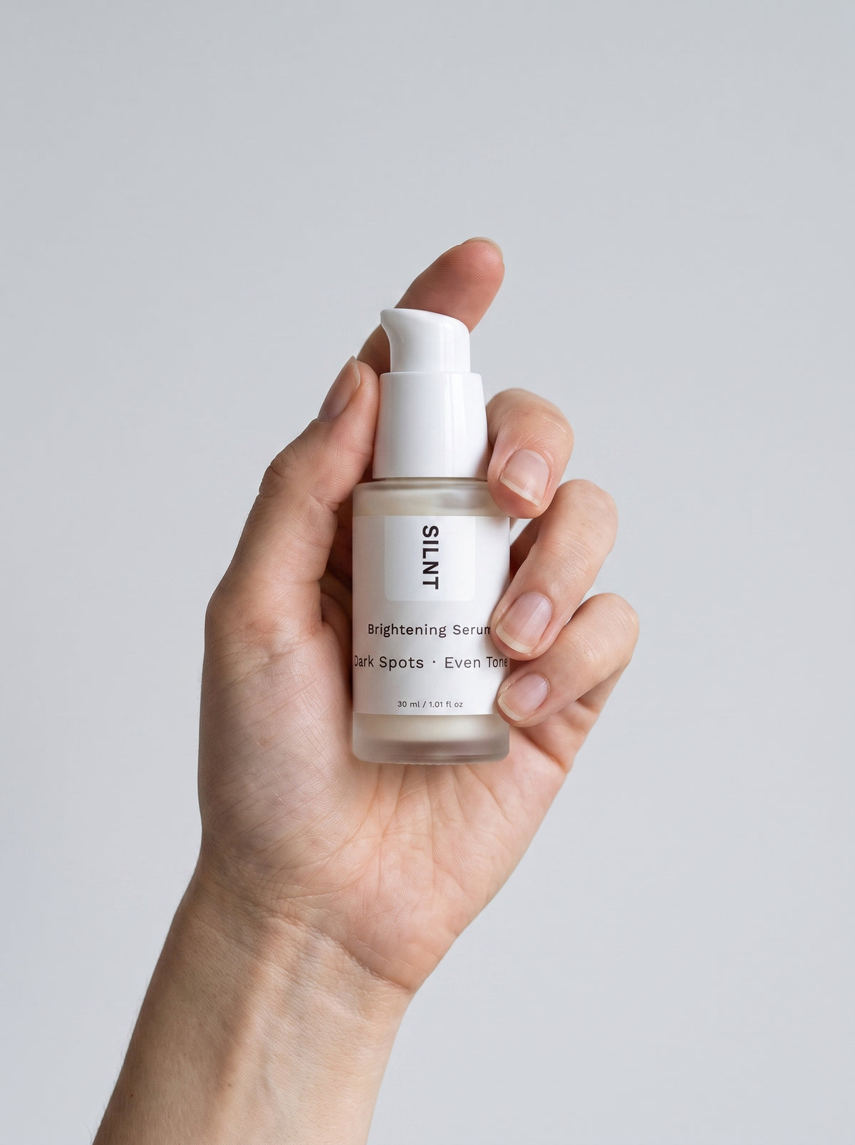 SILNT Brightening Serum bottle held upright in one hand against a light grey background