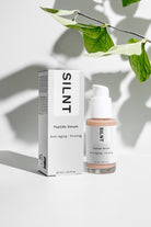 SILNT Peptide Serum bottle beside its carton with soft leaf shadows