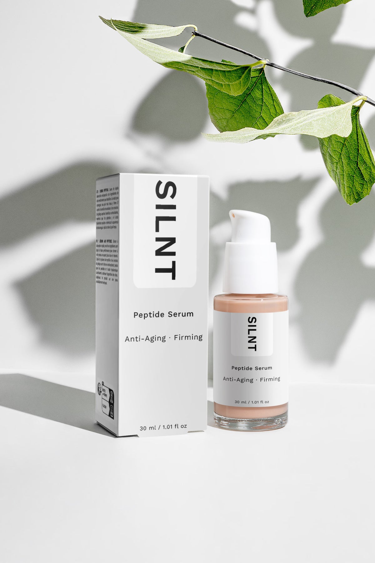 SILNT Peptide Serum bottle beside its carton with soft leaf shadows