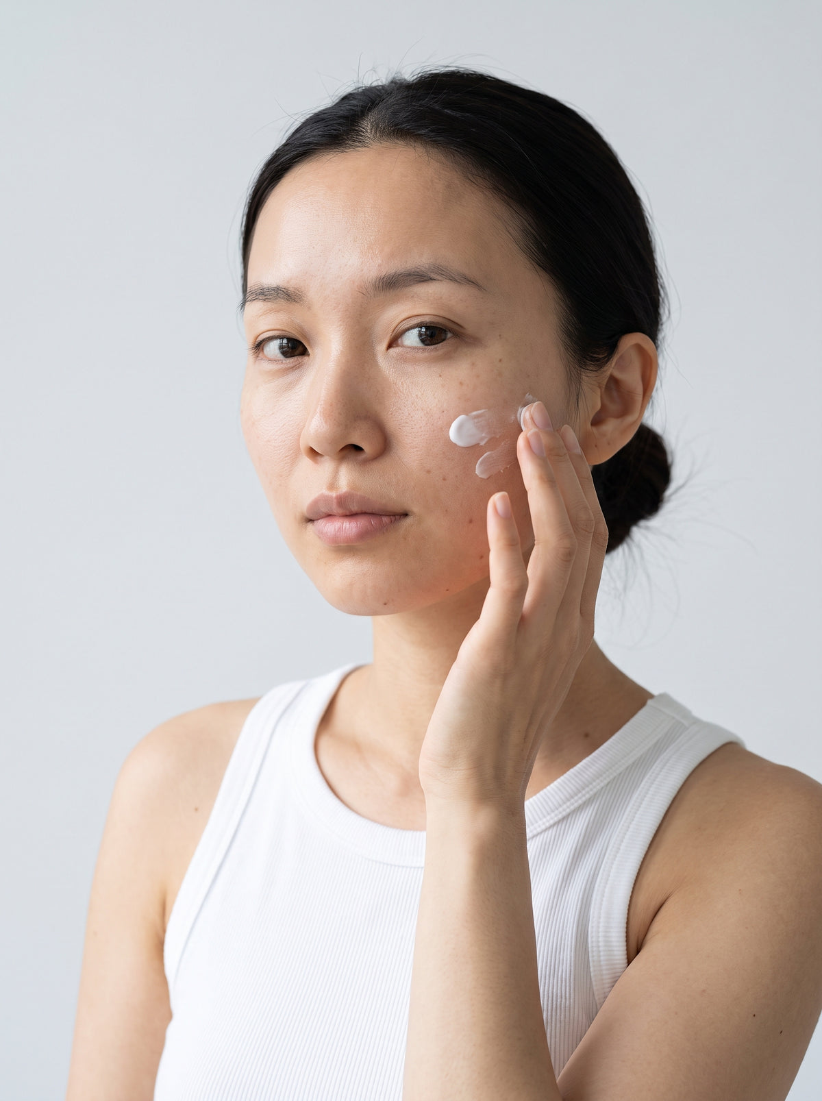 SILNT Overnight Cream applied to a model's cheek with her fingertips, white tank top, light grey background