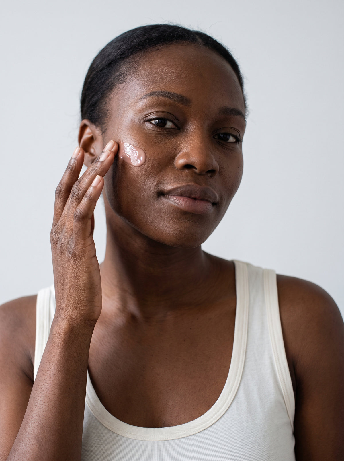 SILNT Peptide Serum applied to a model's cheek with her fingertips, white tank top, light grey background
