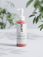 SILNT Radiance Cleanser bottle beside its carton with soft leaf shadows on a light grey background