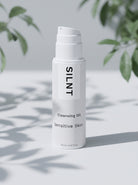 SILNT Cleansing Oil bottle beside soft leaf shadows on a light grey background