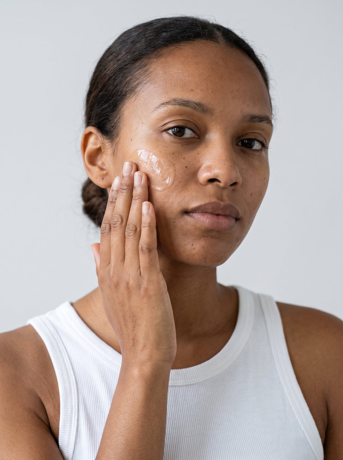 SILNT Hydration Gel applied to a model's cheek with her fingertips, white tank top, light grey background