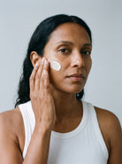 SILNT Day Cream applied to a model's cheek with her fingertips, white tank top, light grey background