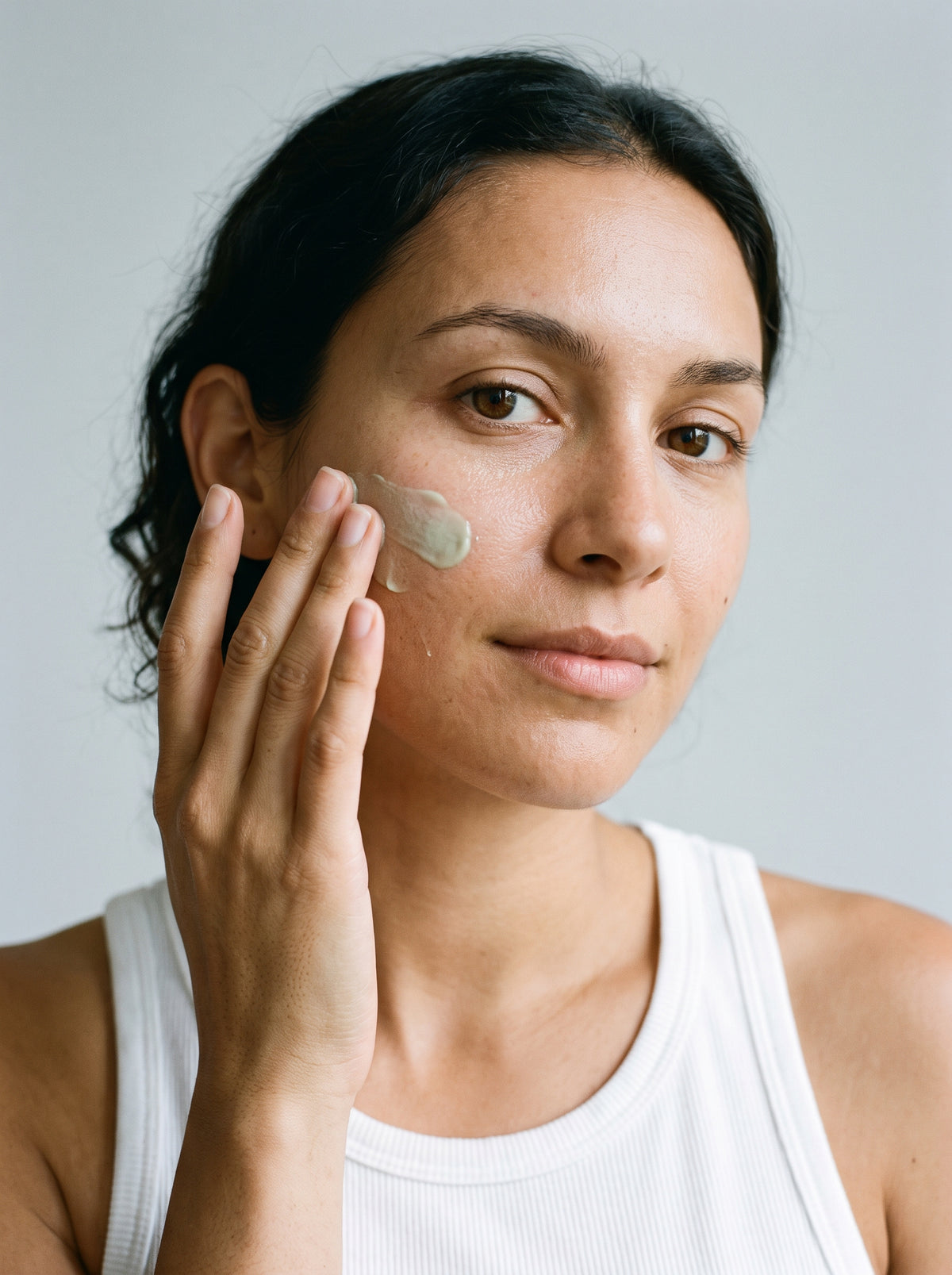SILNT Clarifying Moisturiser applied to a model's cheek with her fingertips, white tank top, light grey background