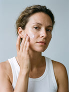 SILNT Retinol Alternative Cream applied to a model's cheek with her fingertips, white tank top, light grey background