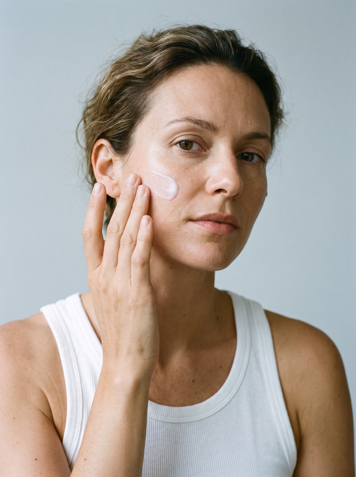 SILNT Retinol Alternative Cream applied to a model's cheek with her fingertips, white tank top, light grey background