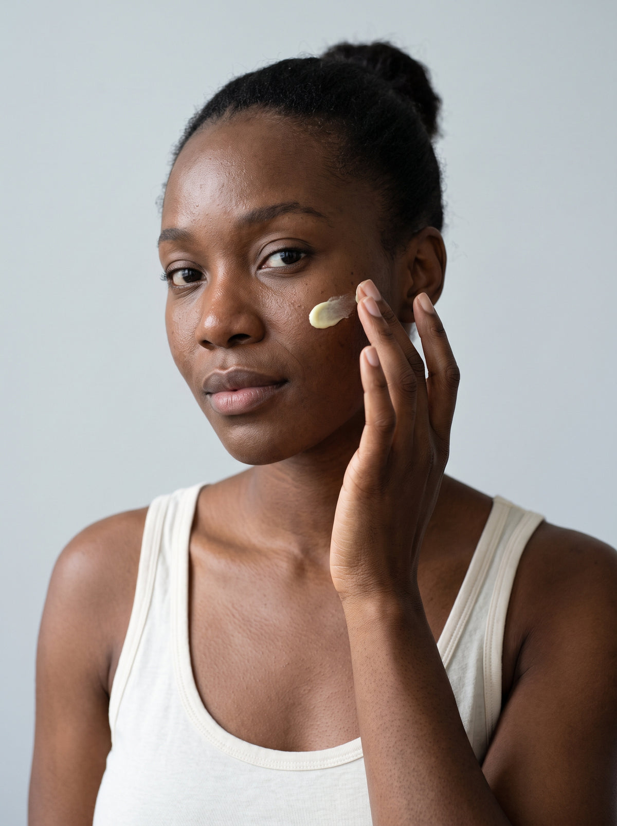 Black woman in a white tank top applying SILNT Vitamin C Serum to her cheek
