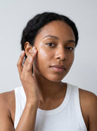 SILNT Exfoliating Concentrate smoothed along a model's cheekbone, white tank top, light grey background