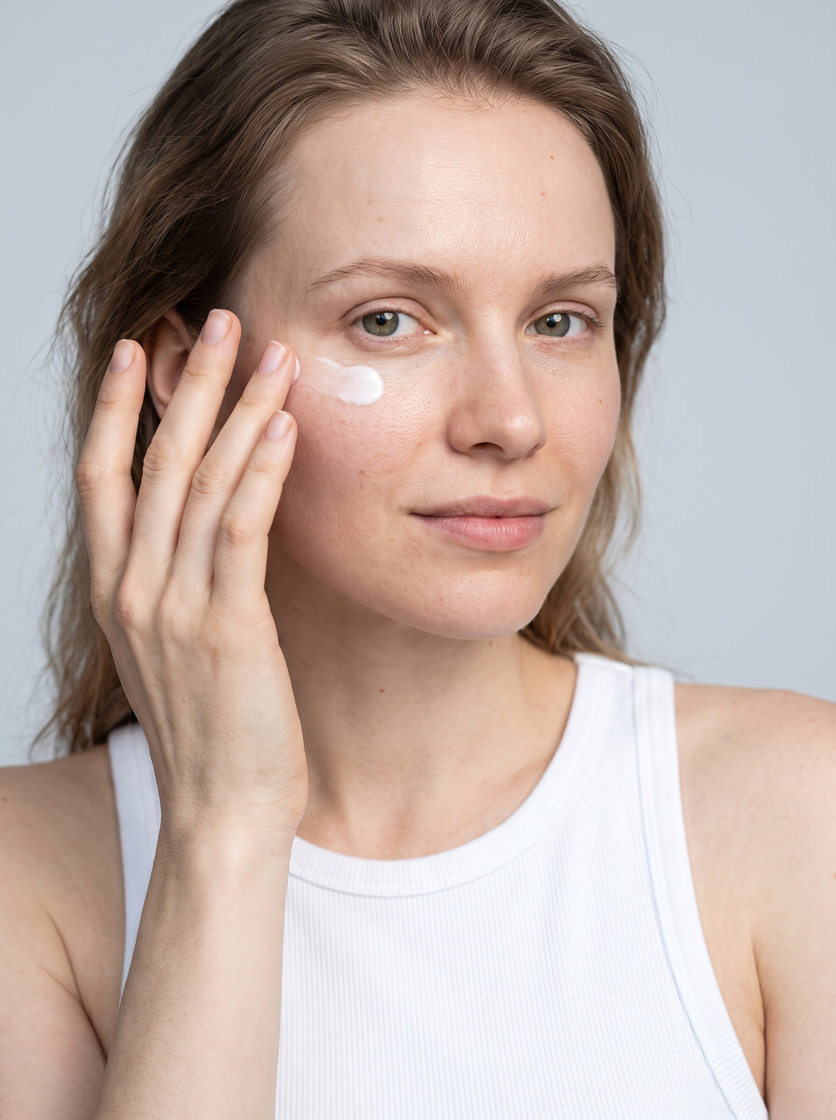 SILNT Eye Cream patted under a model's eye with her ring fingertip, white tank top, light grey background