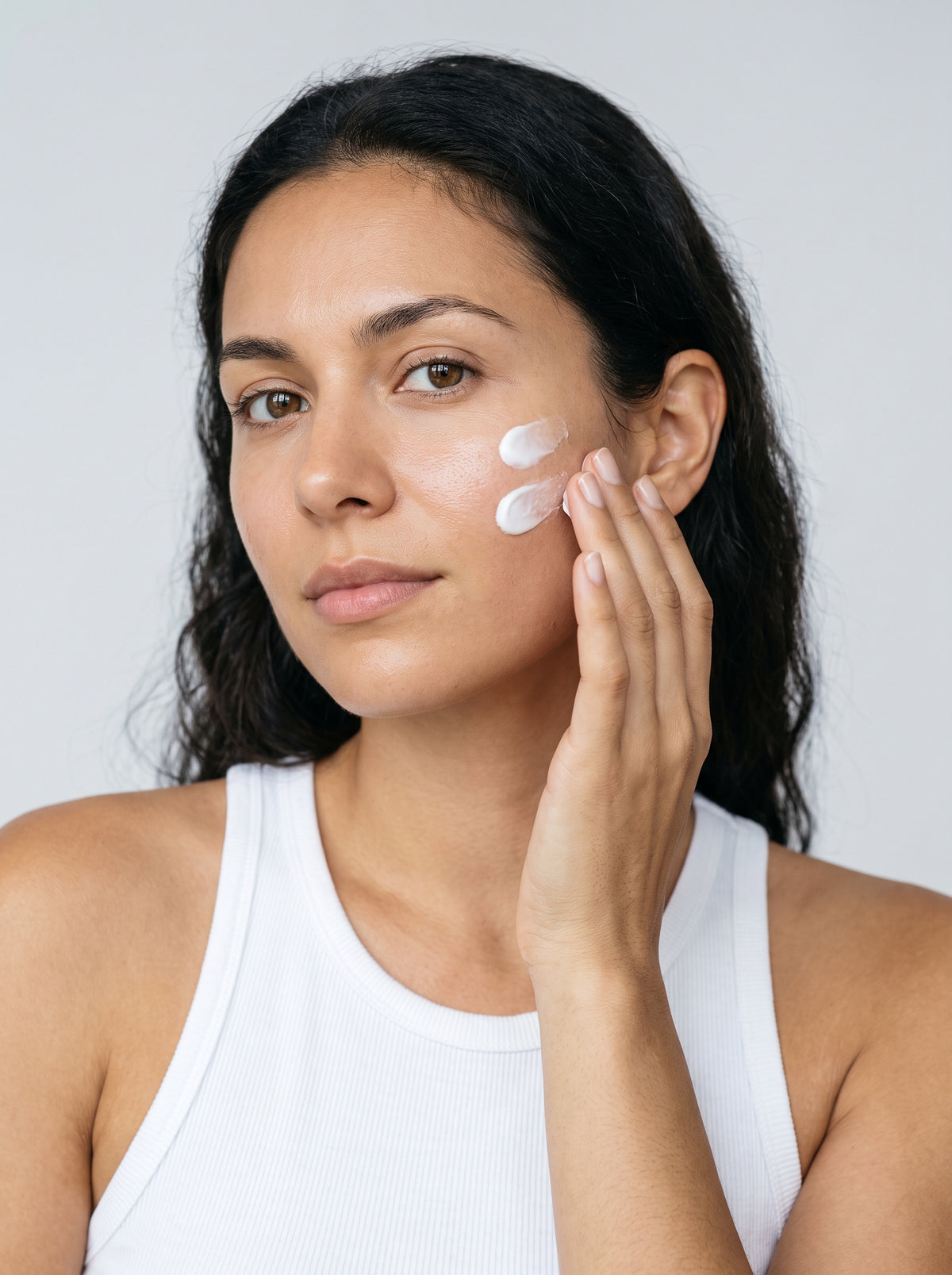 SILNT Daily Moisturizer applied to a model's cheek with her fingertips, white tank top, light grey background