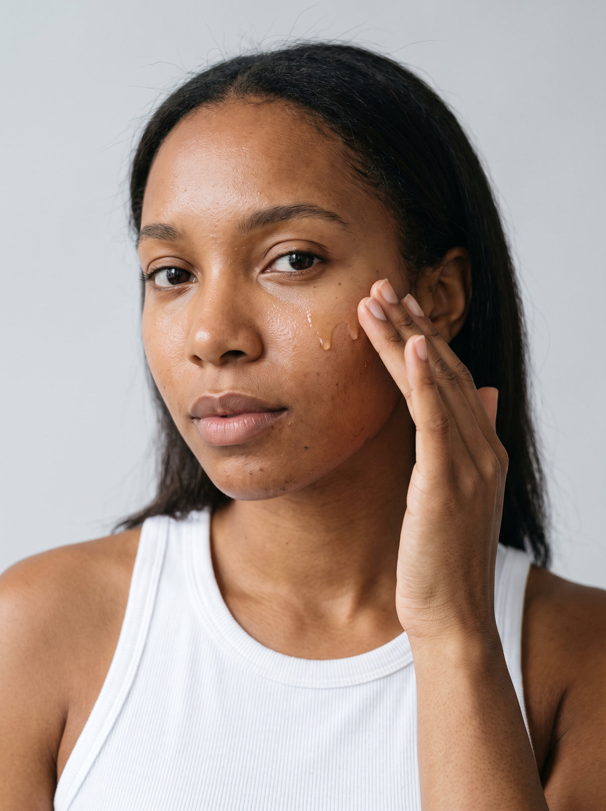 SILNT Facial Oil pressed into a model's cheek with her fingertips, white tank top, light grey background