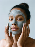 SILNT Clarifying Mask grey clay applied over a model's face with her fingertips, light grey background