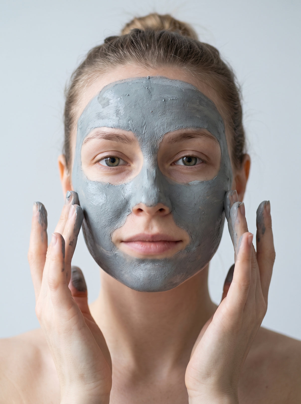 SILNT Clarifying Mask grey clay applied over a model's face with her fingertips, light grey background