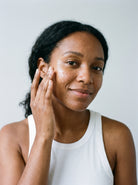 Woman in a white tank top applying SILNT Prebiotic Serum to her cheek