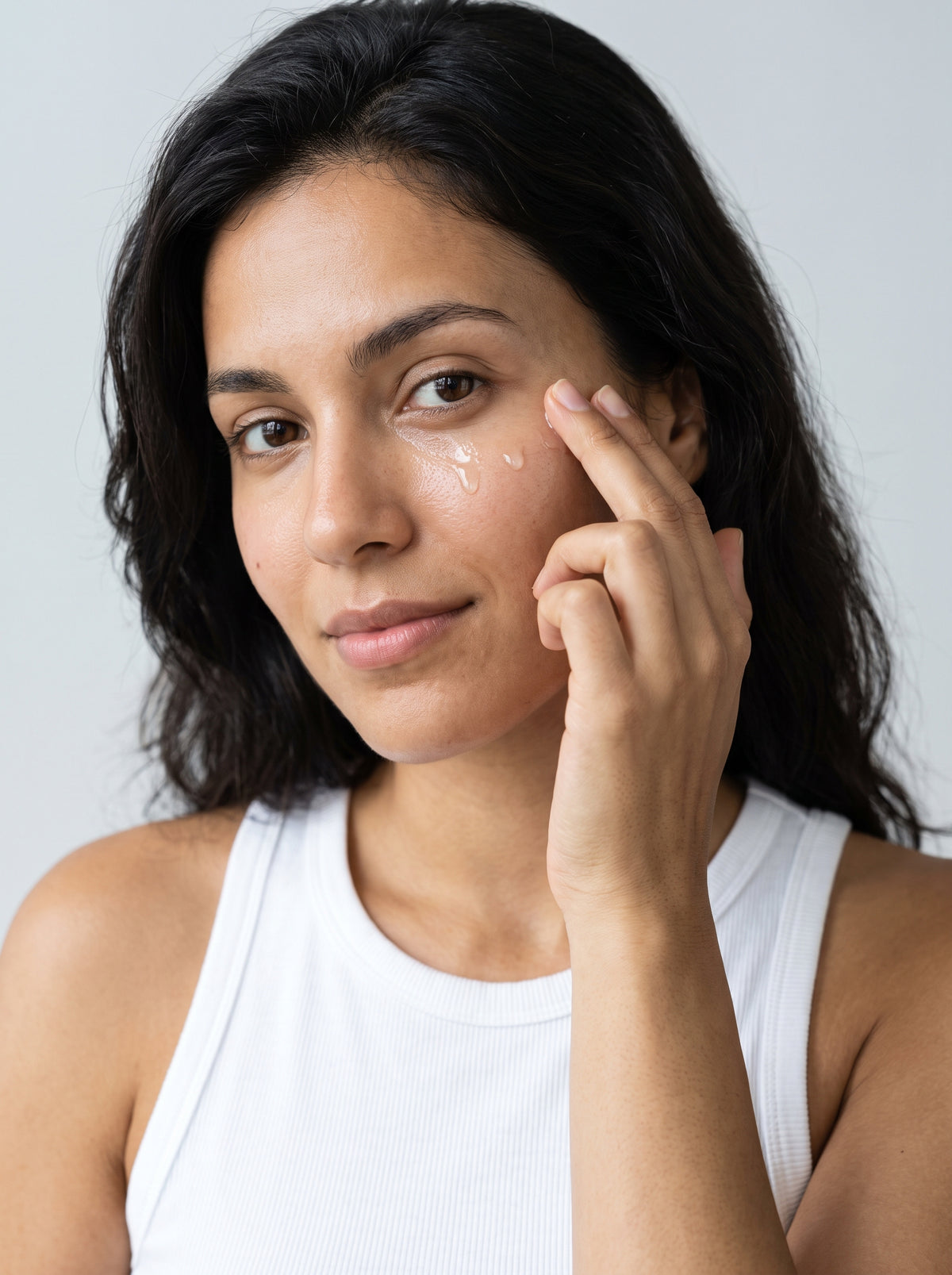Woman in a white tank top pressing SILNT Caffeine Booster around her eye