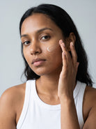 SILNT Brightening Serum applied to a model's cheek with her fingertips, white tank top, light grey background