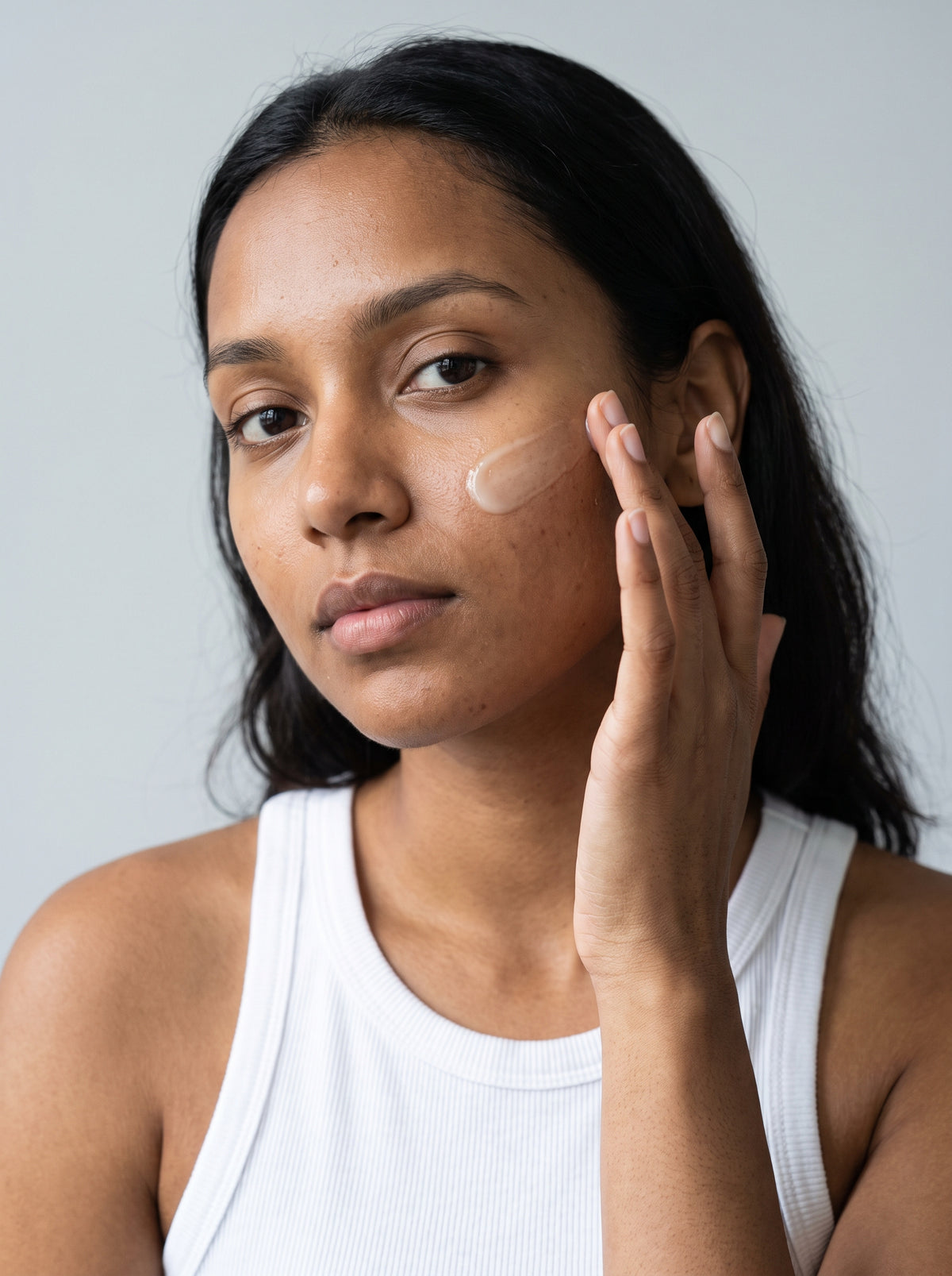 SILNT Brightening Serum applied to a model's cheek with her fingertips, white tank top, light grey background