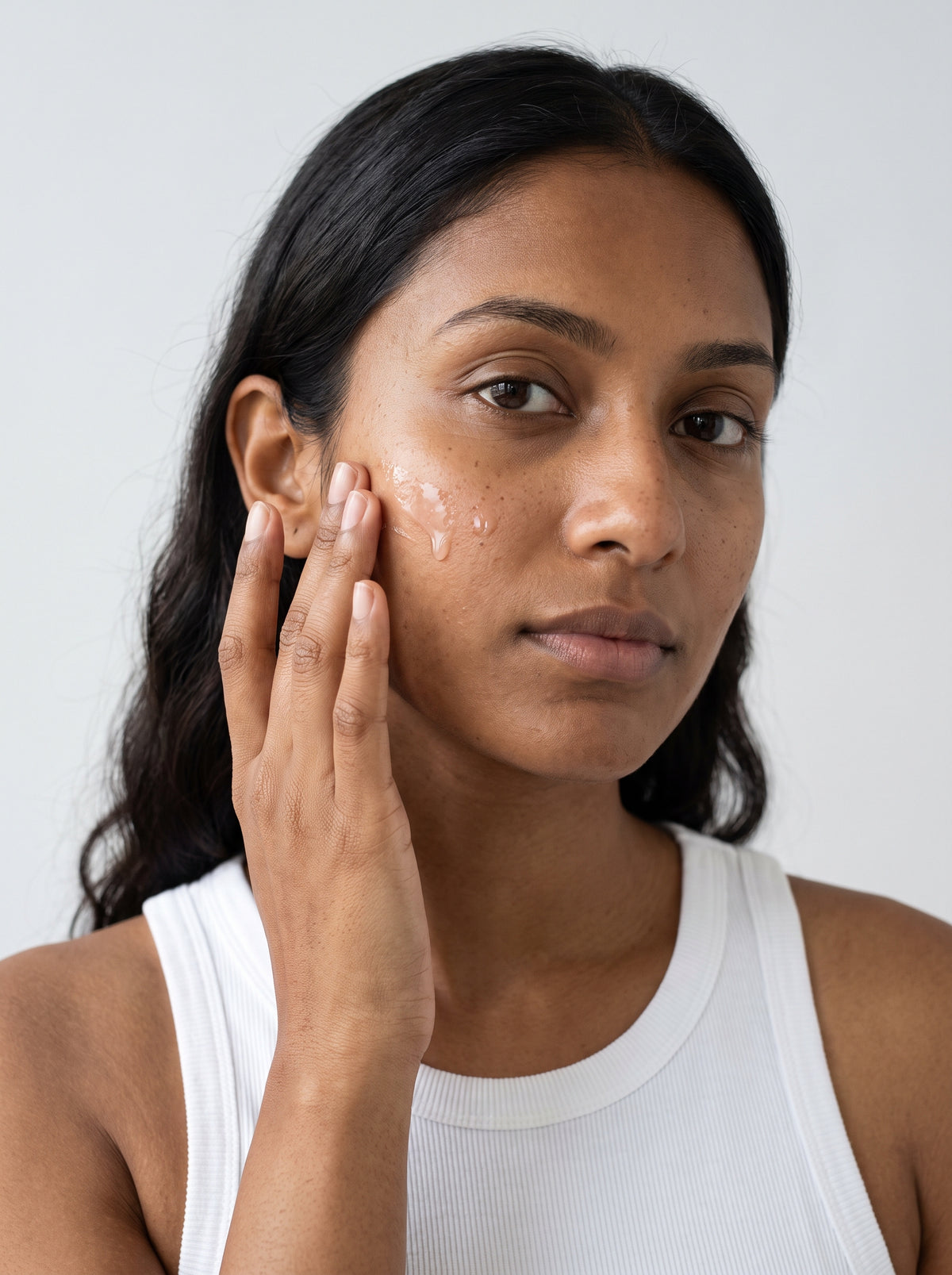 SILNT Hydrating Serum smoothed along a model's cheekbone, white tank top, light grey background