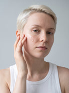 SILNT Hydrating Serum applied to a model's cheek with her fingertips, white tank top, light grey background