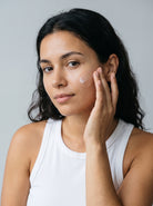 SILNT Plumping Serum smoothed along a model's cheekbone, white tank top, light grey background