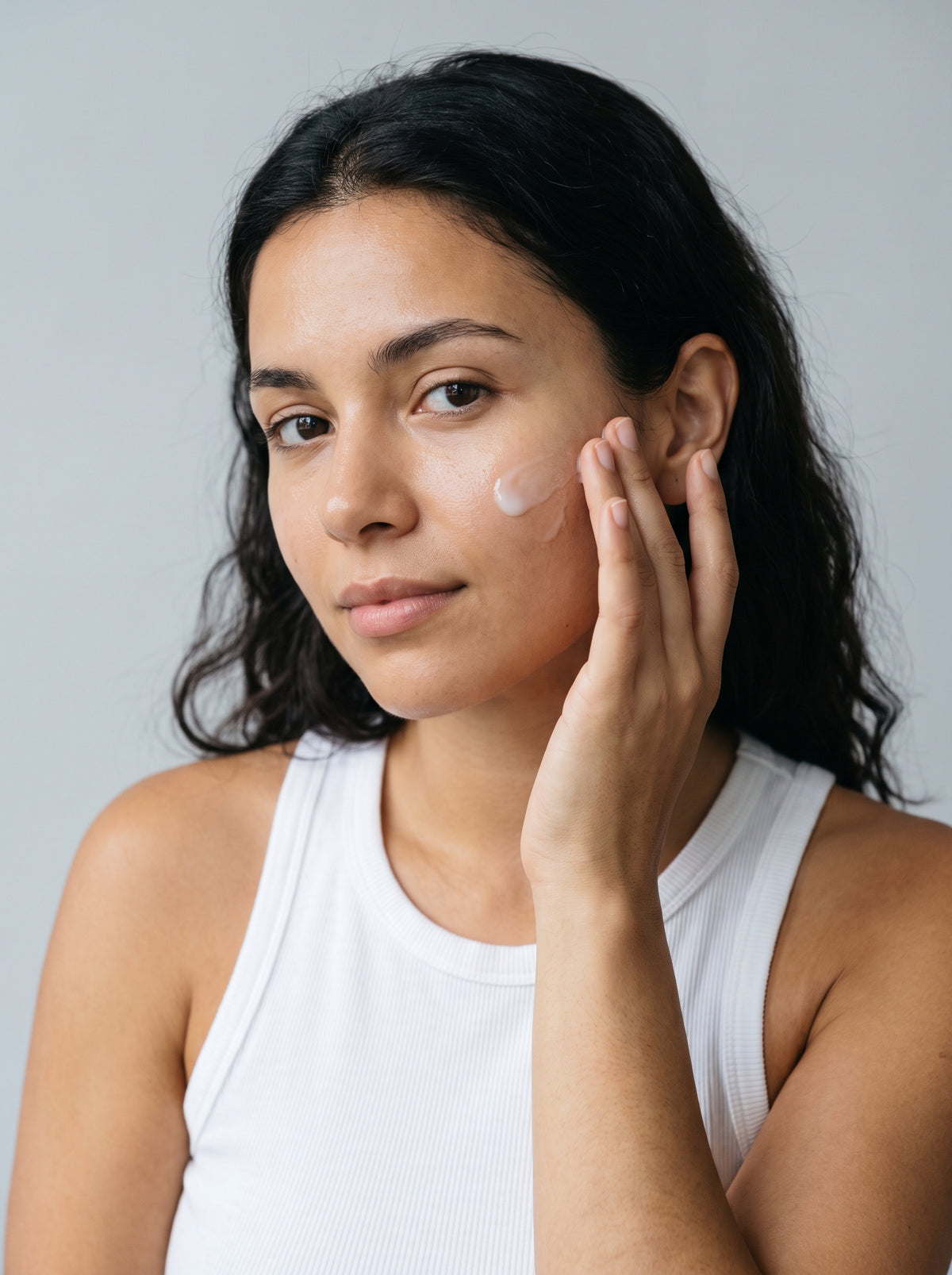 SILNT Plumping Serum smoothed along a model's cheekbone, white tank top, light grey background